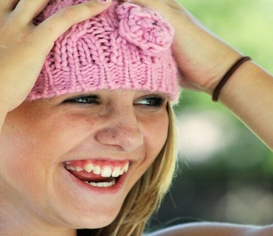 Niña rubia con sombrero de lana rosa, las manos en la cabeza y sonriendo.